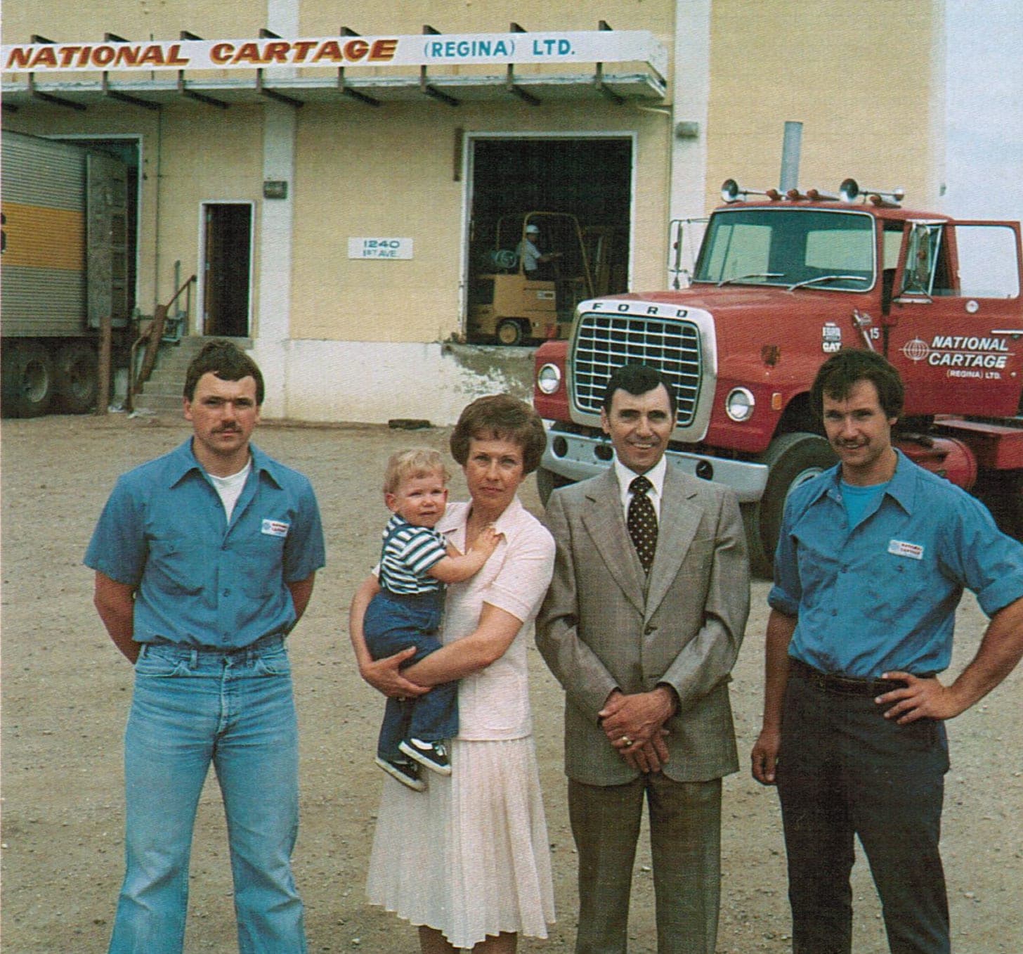 John, Lorraine holding Tyler, Al, and Brian Yaehne standing with a National Cartage truck outside the Regina terminal in 1981